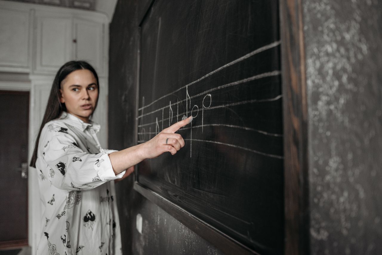 our-experience A music teacher explaining musical notes on a blackboard inside a classroom.