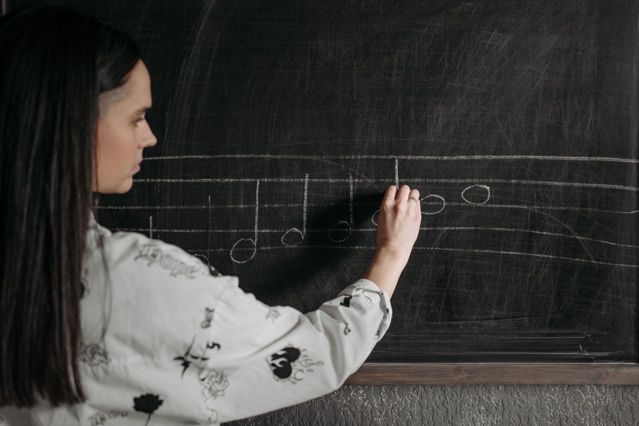 about-img A woman writing music notation on a blackboard during a lesson.