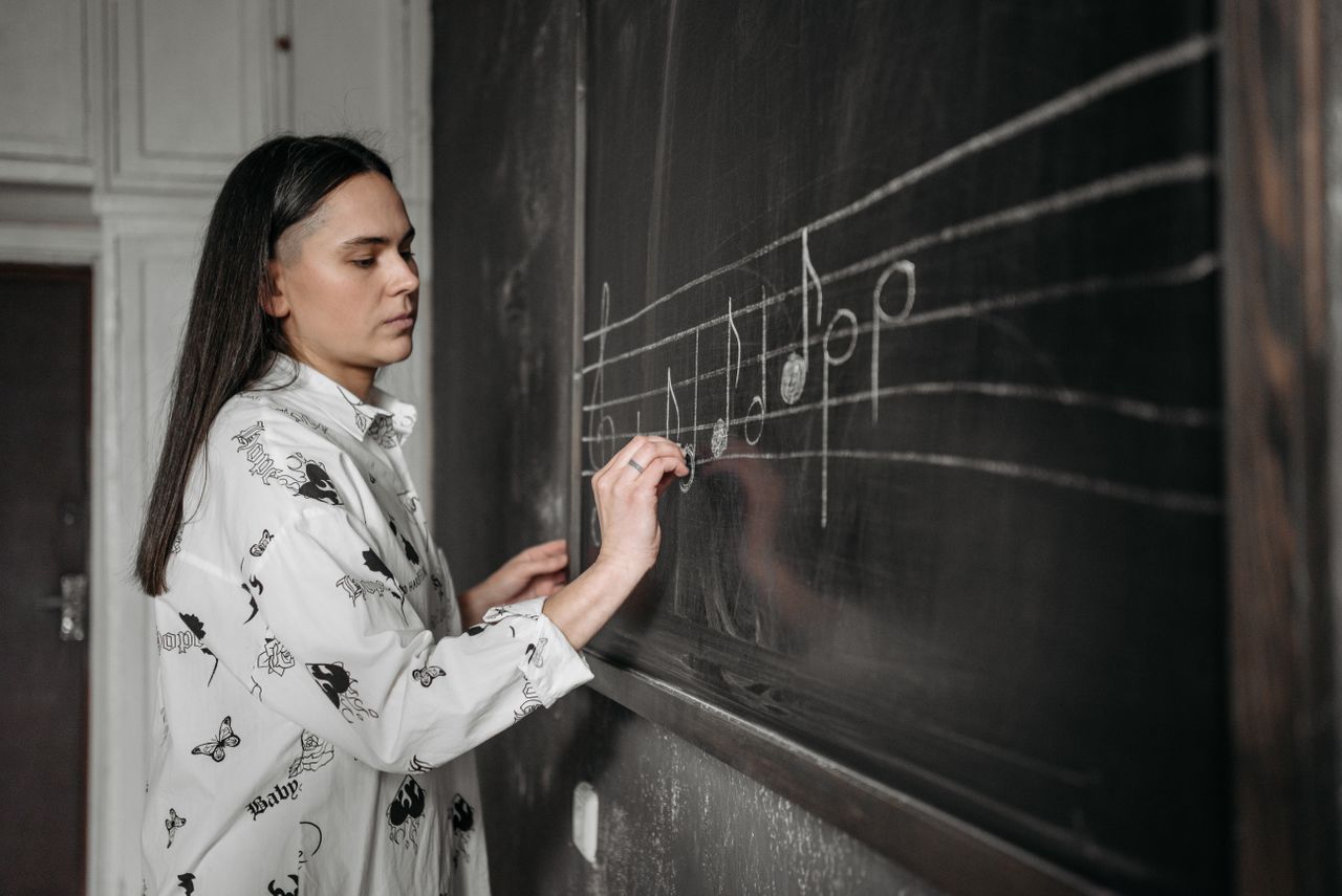 Mastering the First Impression: Your intriguing post title goes here A woman drawing musical notes on a chalkboard in a classroom setting.