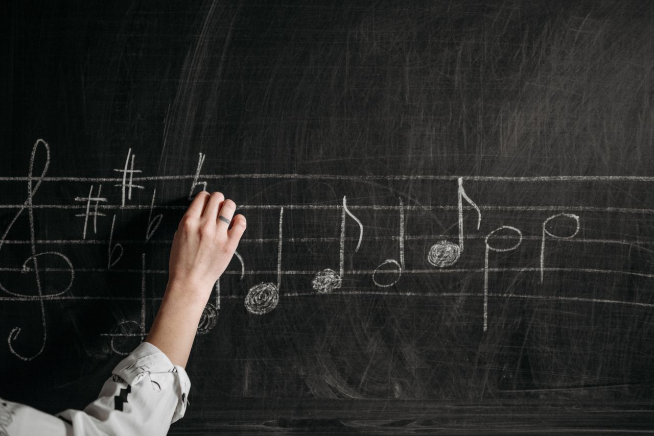 Crafting Captivating Headlines: Your awesome post title goes here A person writing musical notes on a blackboard with chalk indoors.