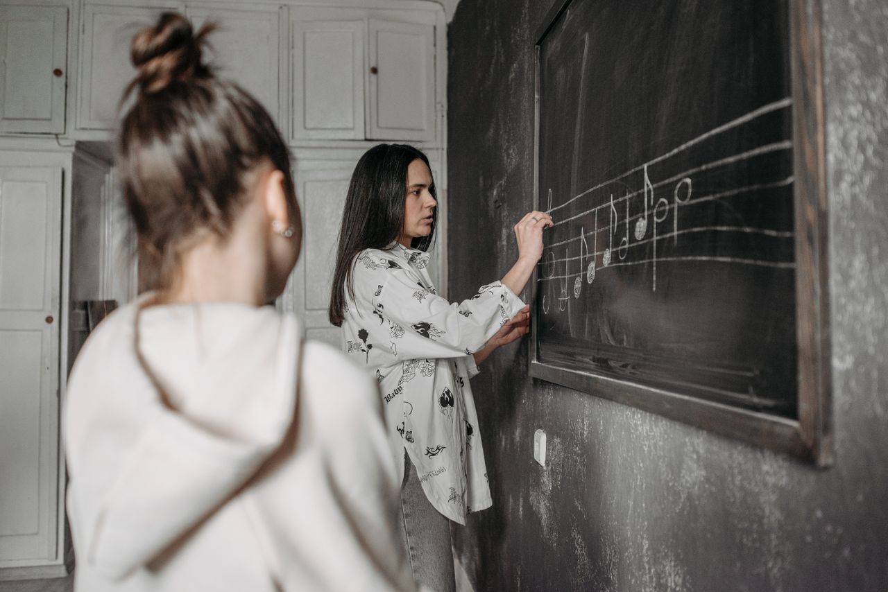 about-02 A student observes a teacher writing music notes on a classroom blackboard.