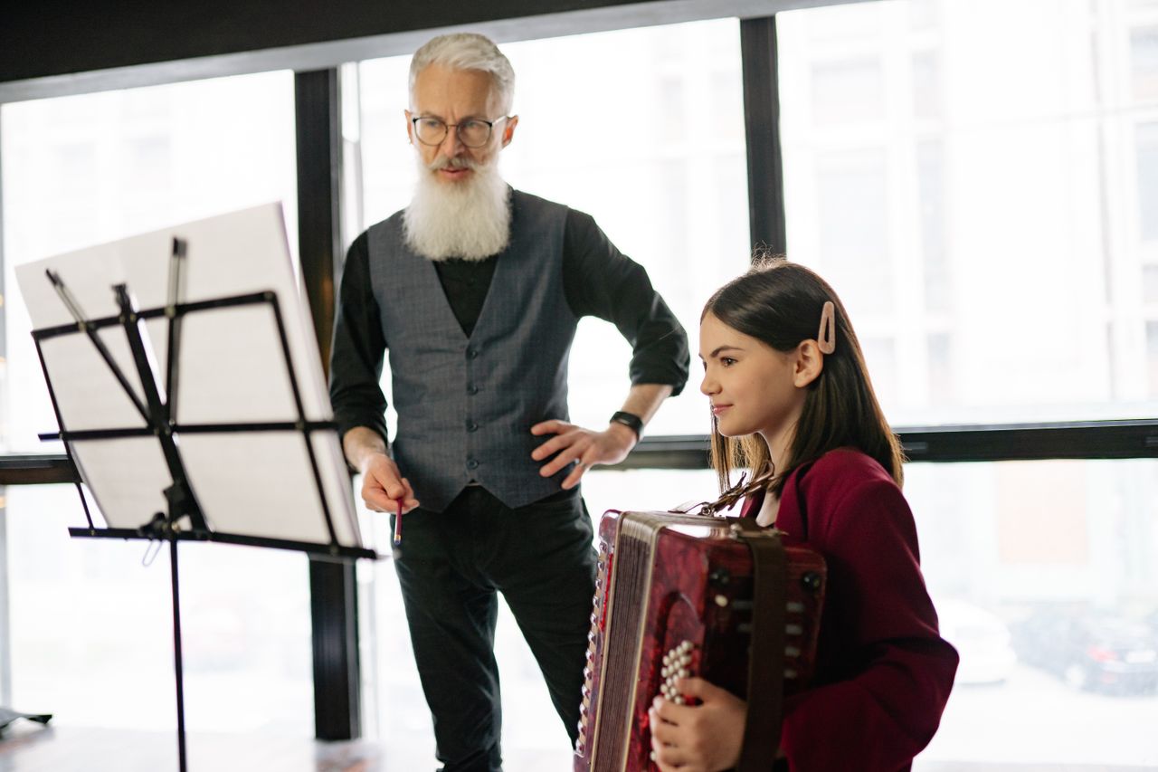 ours-journey A teacher instructing a young girl playing the accordion during a music lesson indoors.