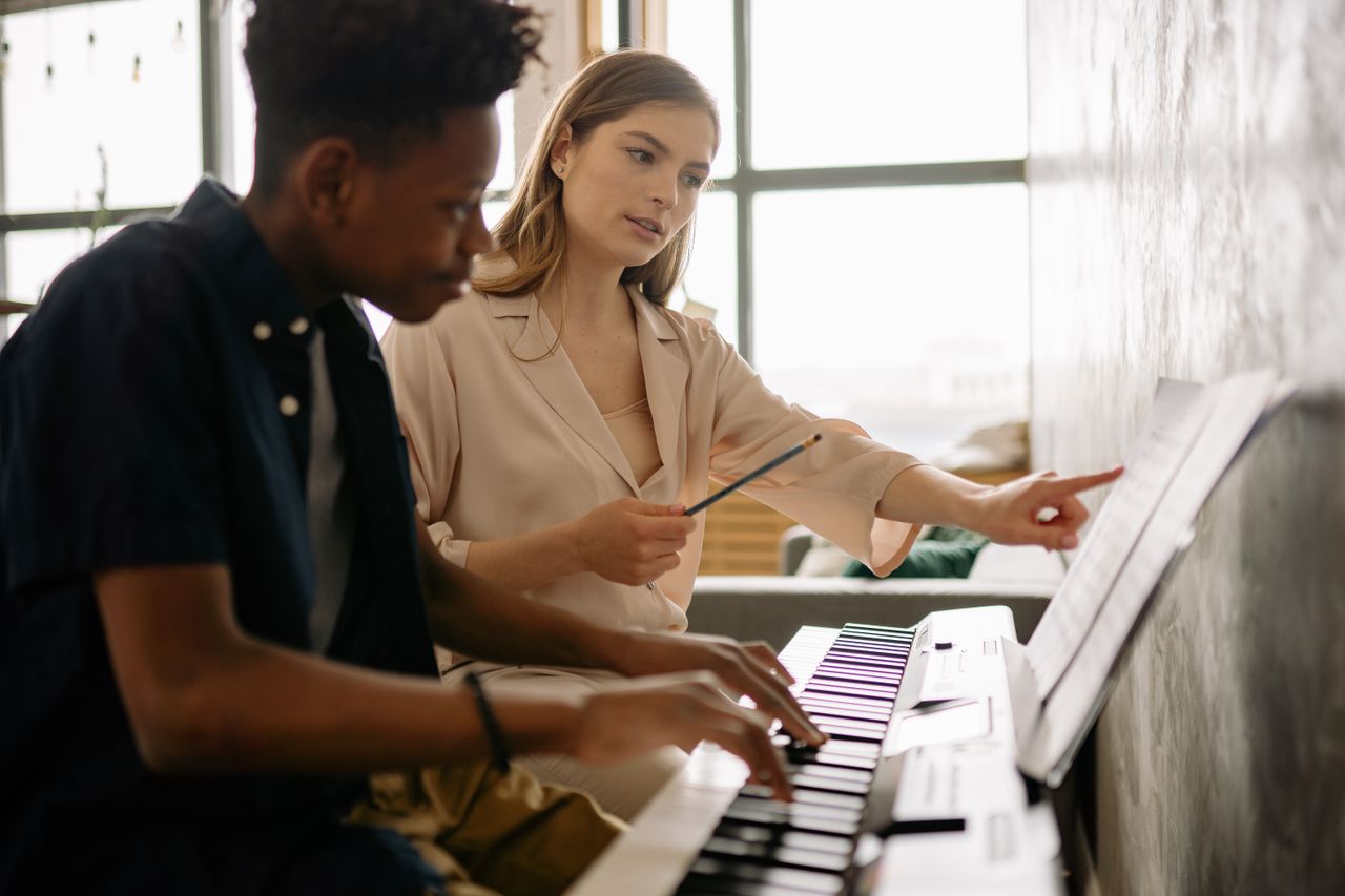 services-04 A teenager learning piano with a teacher at home, focusing on musical notes.